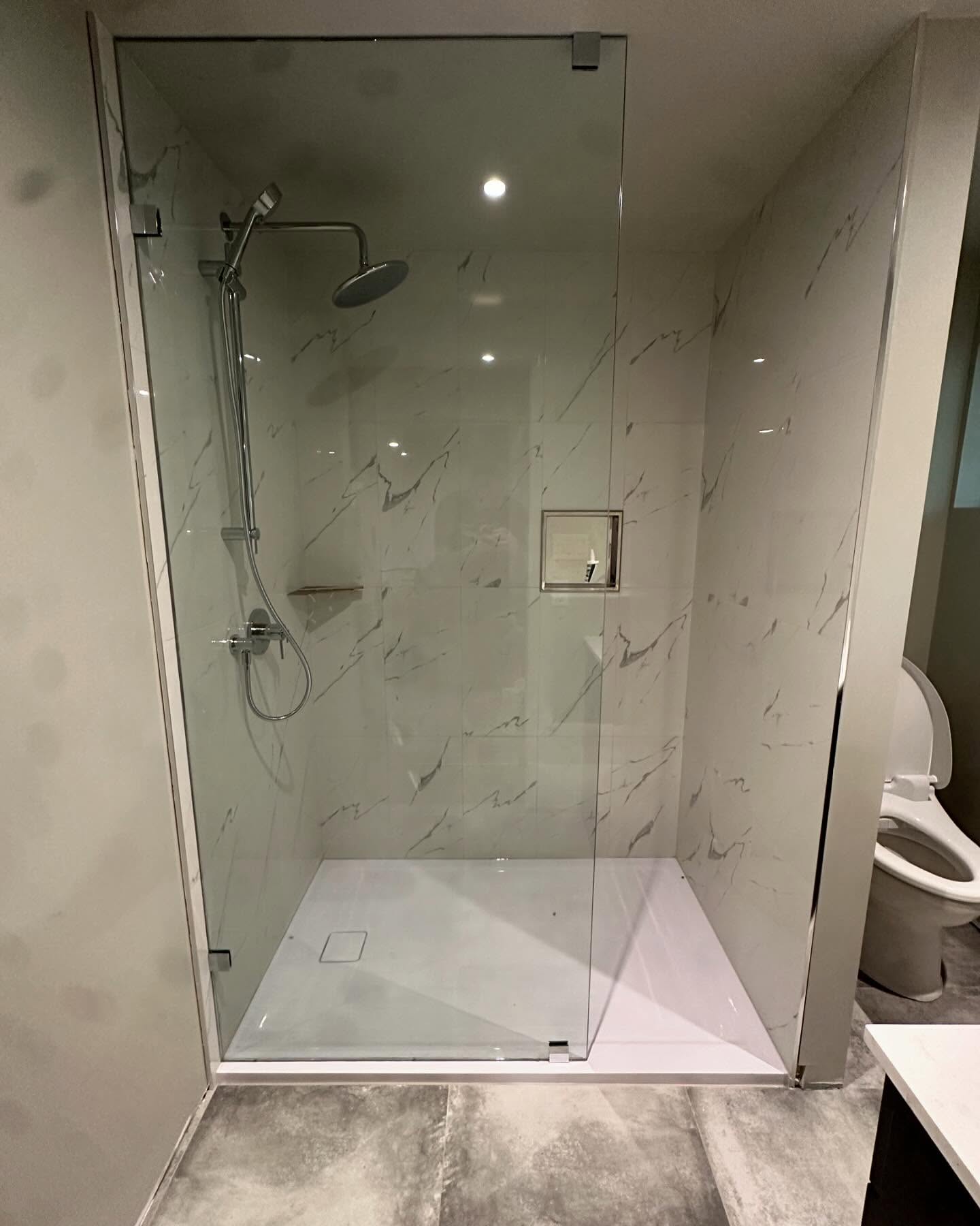 Minimal frameless glass shower screen in a marble tile bathroom